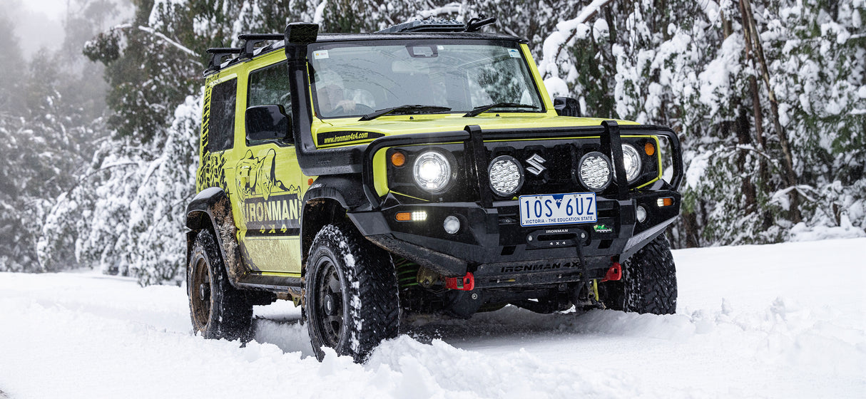 Bright green Suzuki Jimny with snorkel navigating snowy terrain.