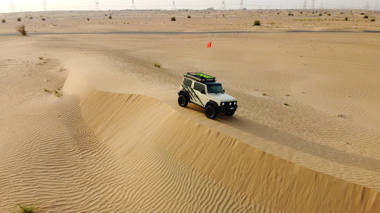 Chiffon Ivory Suzuki Jimny JB74 with Ironman 4x4 accessories driving in Dubai sand dunes.